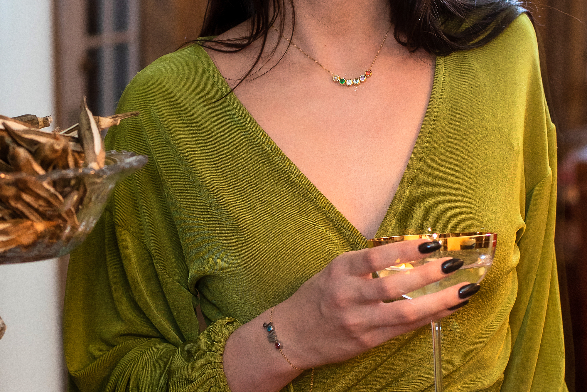 woman holding a glass and wearing a charm necklace and bracelet