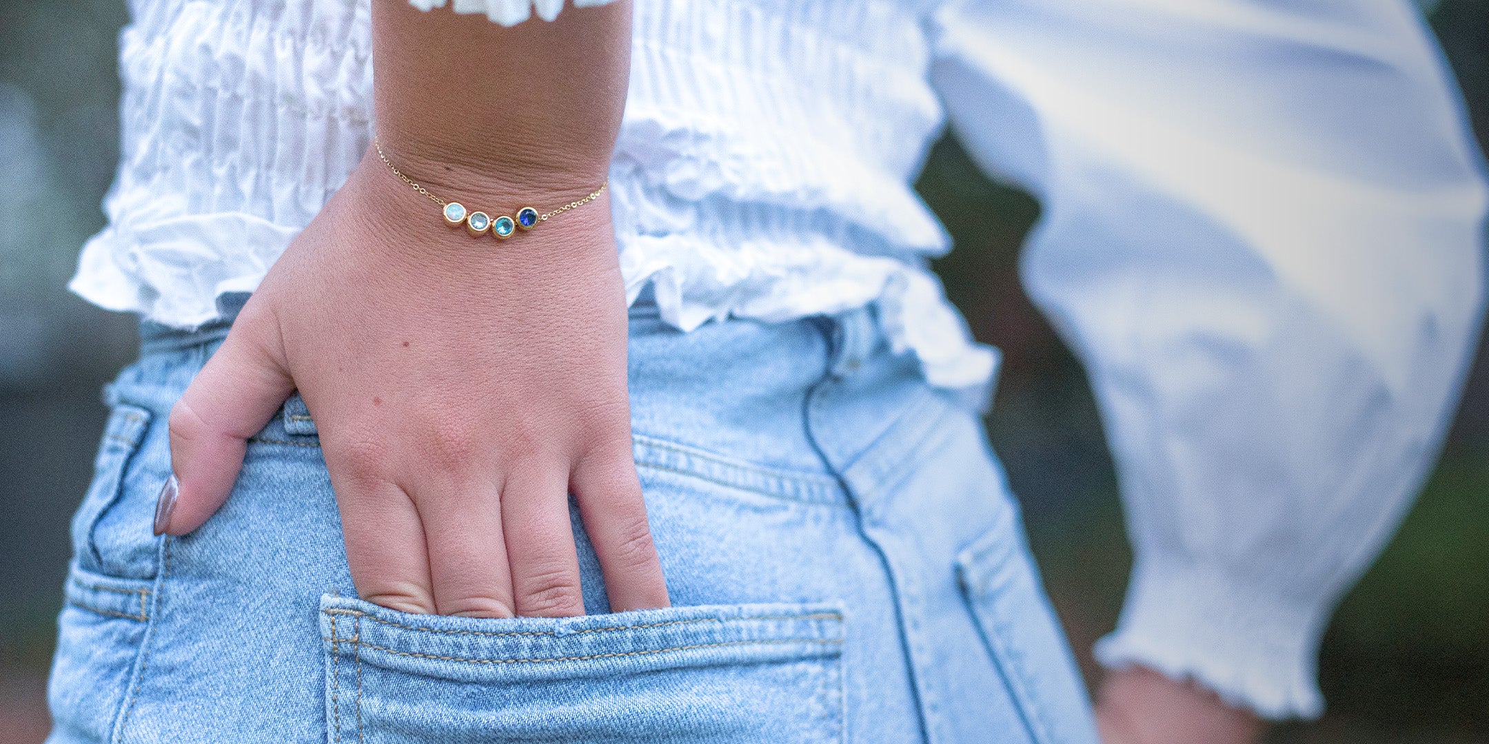 hand in jean pocket wearing gold charm bracelet with blue gems