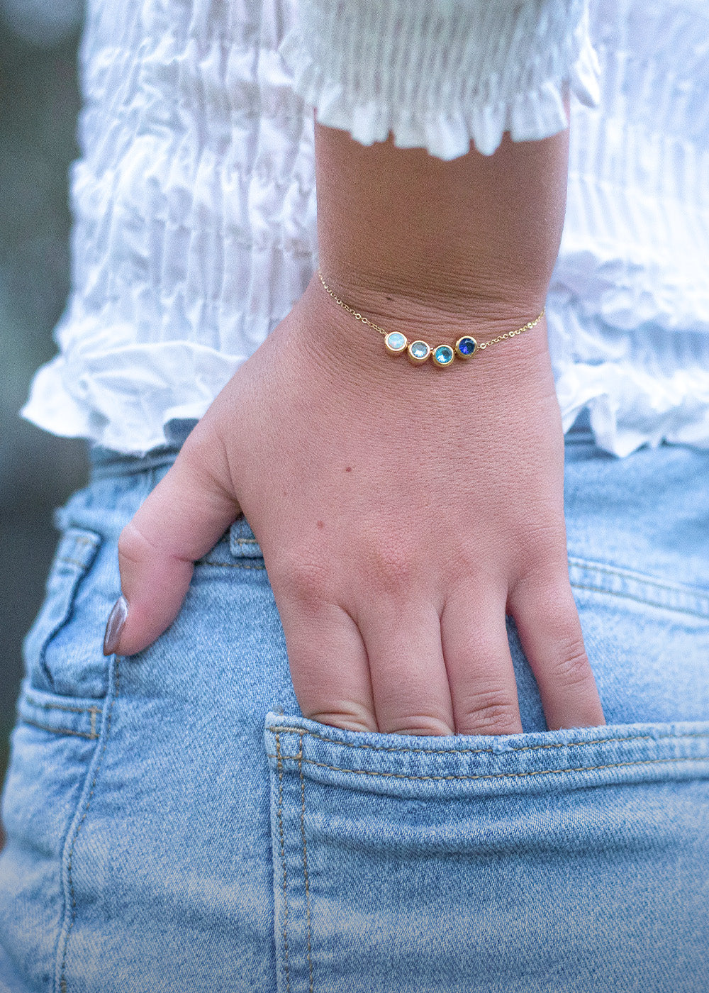 hand in jean pocket wearing gold charm bracelet with blue gems